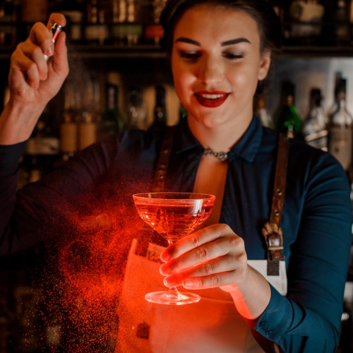 Beautiful bartender girl spraying on the delicious cocktail in her hand